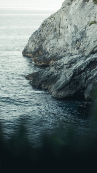Serene view of a rocky coastal cliff with waves gently lapping at the shoreline under a cloudy sky.