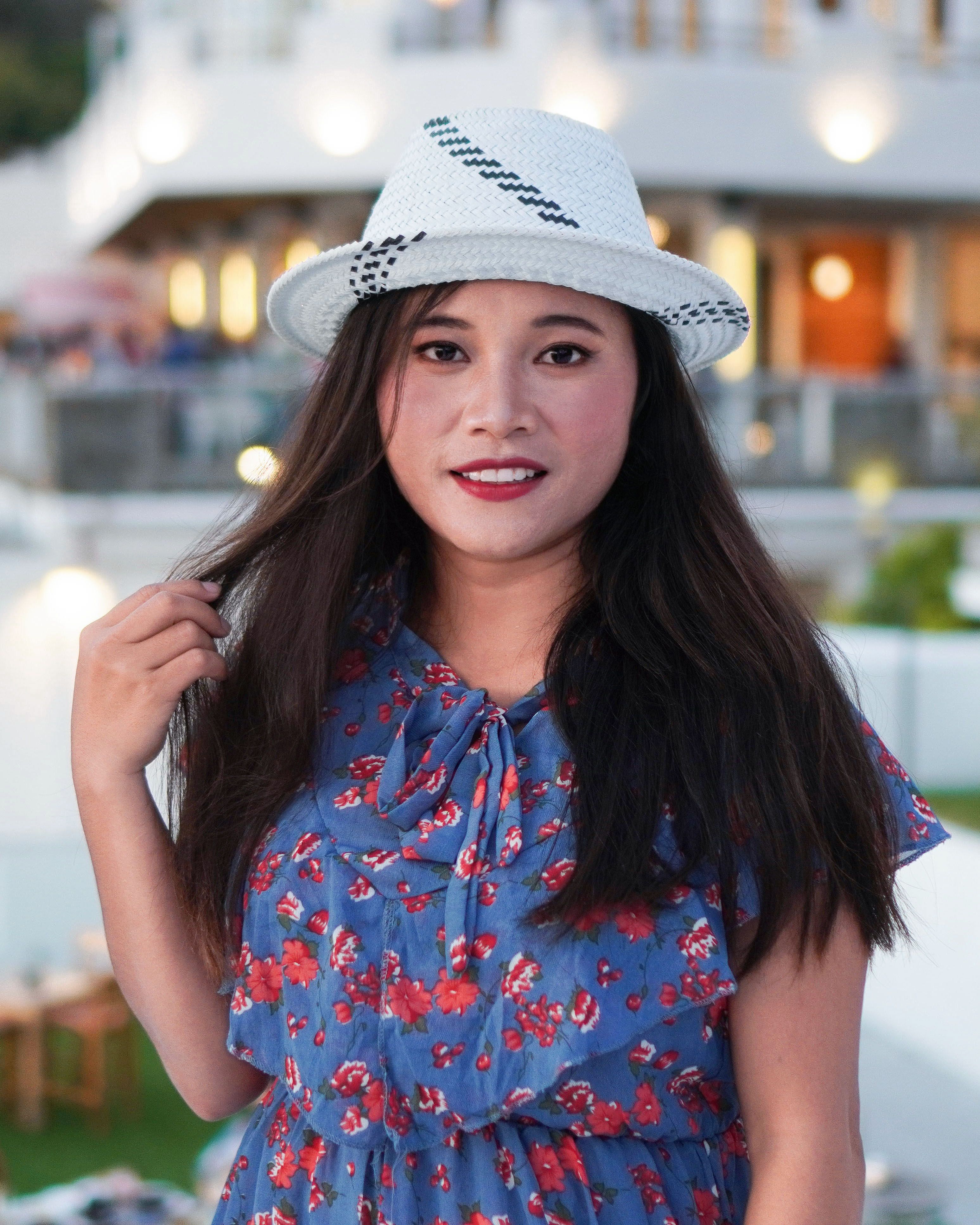 Fashionable asian woman in blue dress and white hat outdoors, showcasing style and elegance.