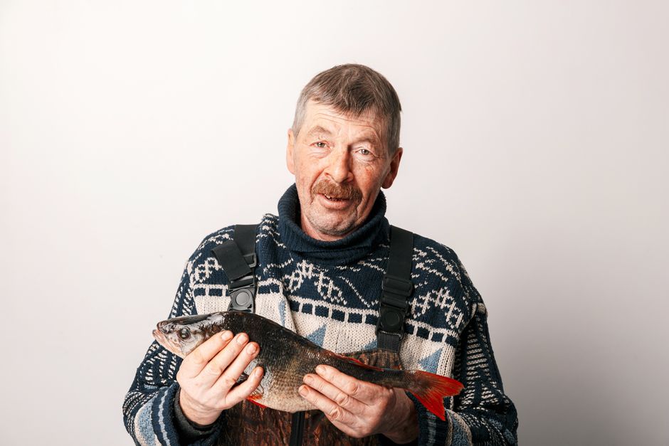 Fotomural Un pescador orgulloso sonríe mientras sostiene un pez recién capturado frente a un fondo neutro.