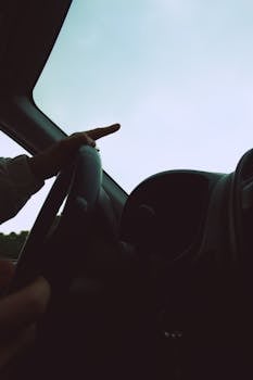 Low-angle view of a person driving a car, capturing the steering wheel and dashboard.