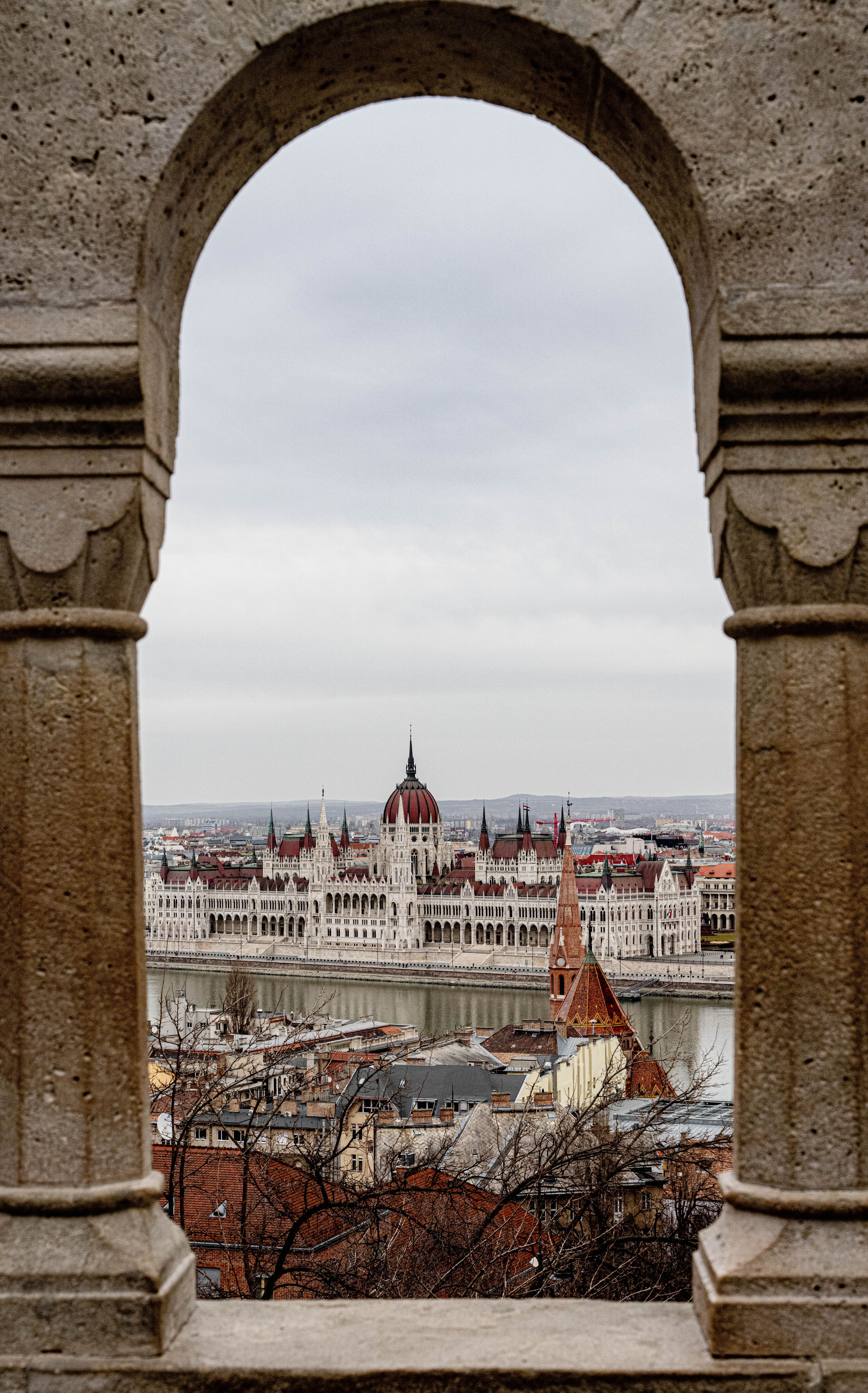 A scenic view of the iconic Budapest Parliament building framed by a historic stone arch.