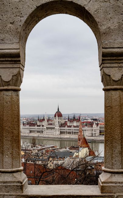 A scenic view of the iconic Budapest Parliament building framed by a historic stone arch.