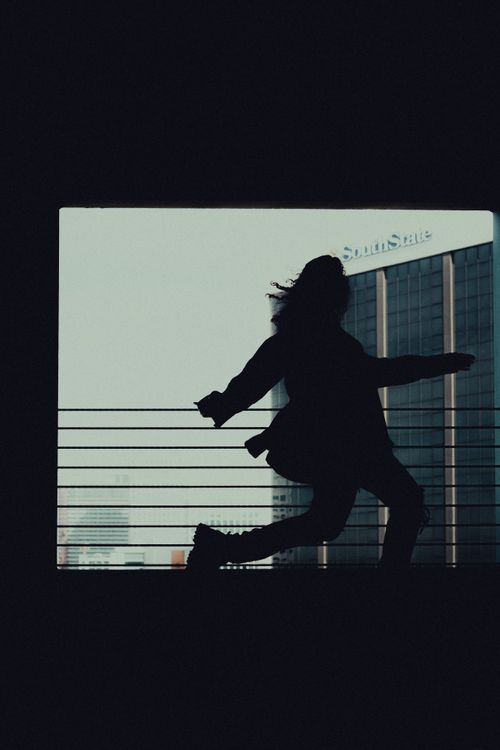 Free A dynamic silhouette of a woman running in an urban environment with a cityscape background. Stock Photo