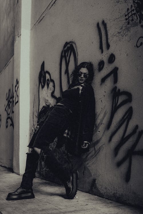 Woman with Sunglasses in Dark Jacket Posing by Graffiti on Wall