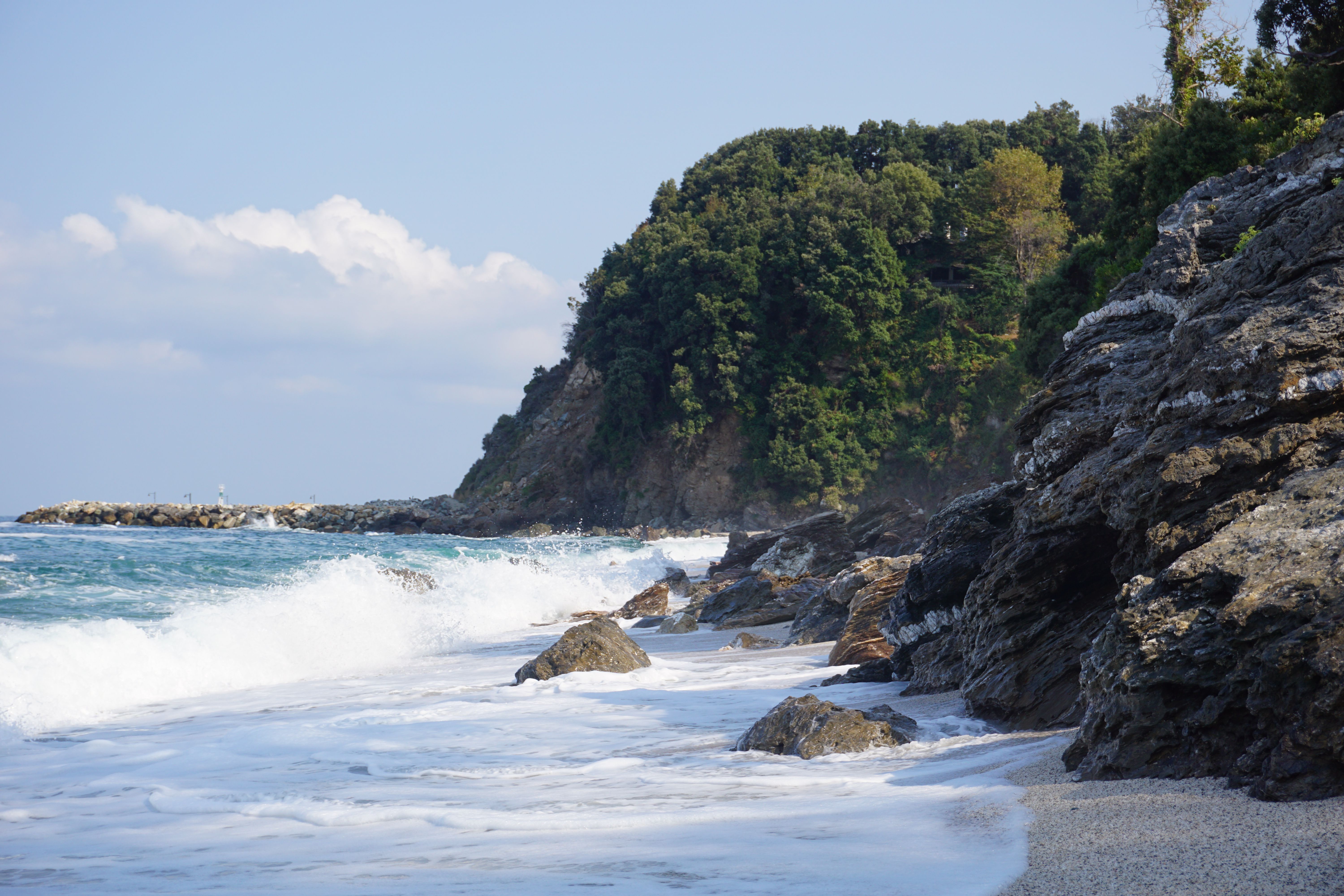 Beautiful rocky coastline with waves crashing onshore under a blue sky.