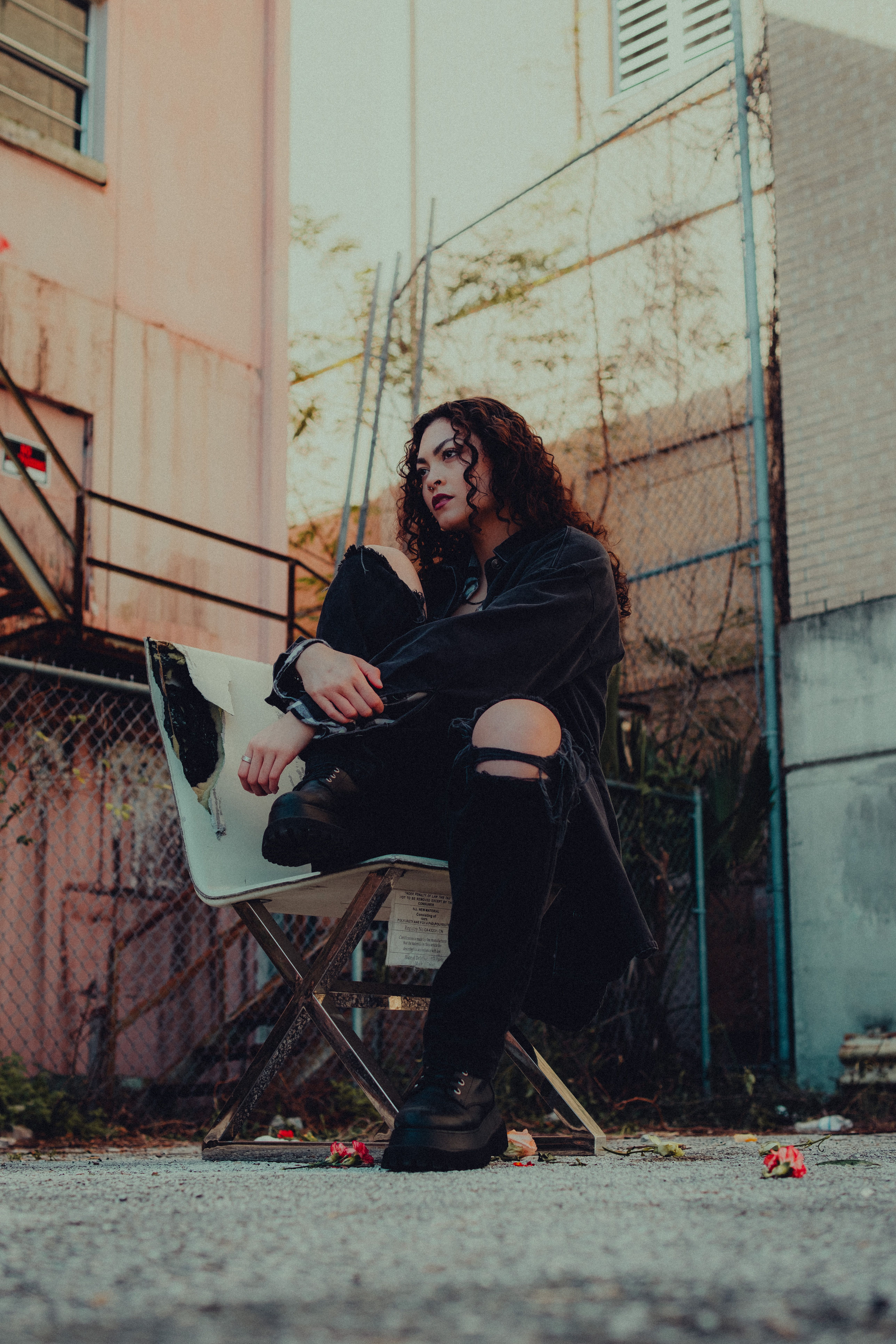model-in-a-black-jacket-and-ripped-jeans-sitting-on-a-chair-in-an-alley