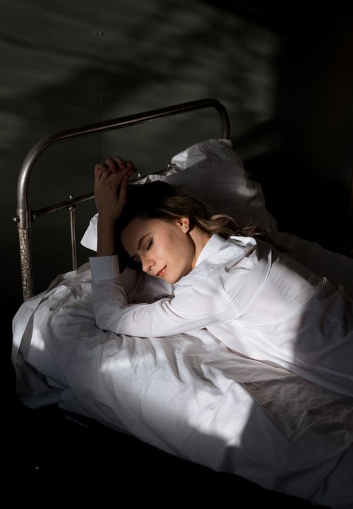 Free A woman peacefully sleeping in bed with gentle sunlight casting shadows, conveying tranquility. Stock Photo