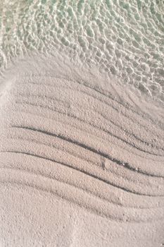 Top-down view of pristine sand and gentle waves on a Maafaru beach, Maldives.