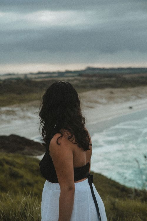 Free Woman in stylish black top and white skirt gazes at beautiful New Zealand seashore view Stock Photo
