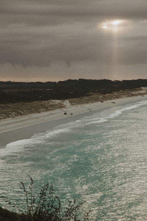 Free A stunning coastal view with sunbeams breaking through clouds over the ocean shore. Stock Photo
