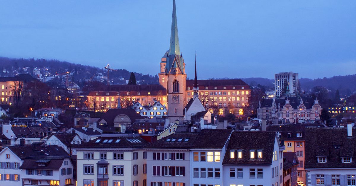 A stunning view of Zurich at dusk featuring illuminated historic buildings and a prominent church spire.