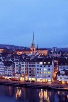 A stunning view of Zurich at dusk featuring illuminated historic buildings and a prominent church spire.