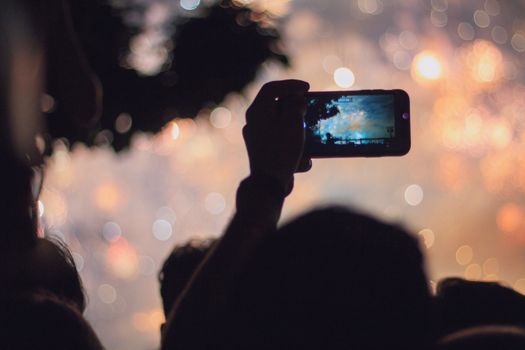 A vibrant night scene of a smartphone capturing fireworks amidst a crowd.