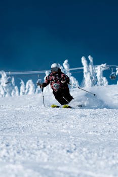 A skier descends a snow-covered mountain slope under a clear blue sky, showcasing winter sports excitement.