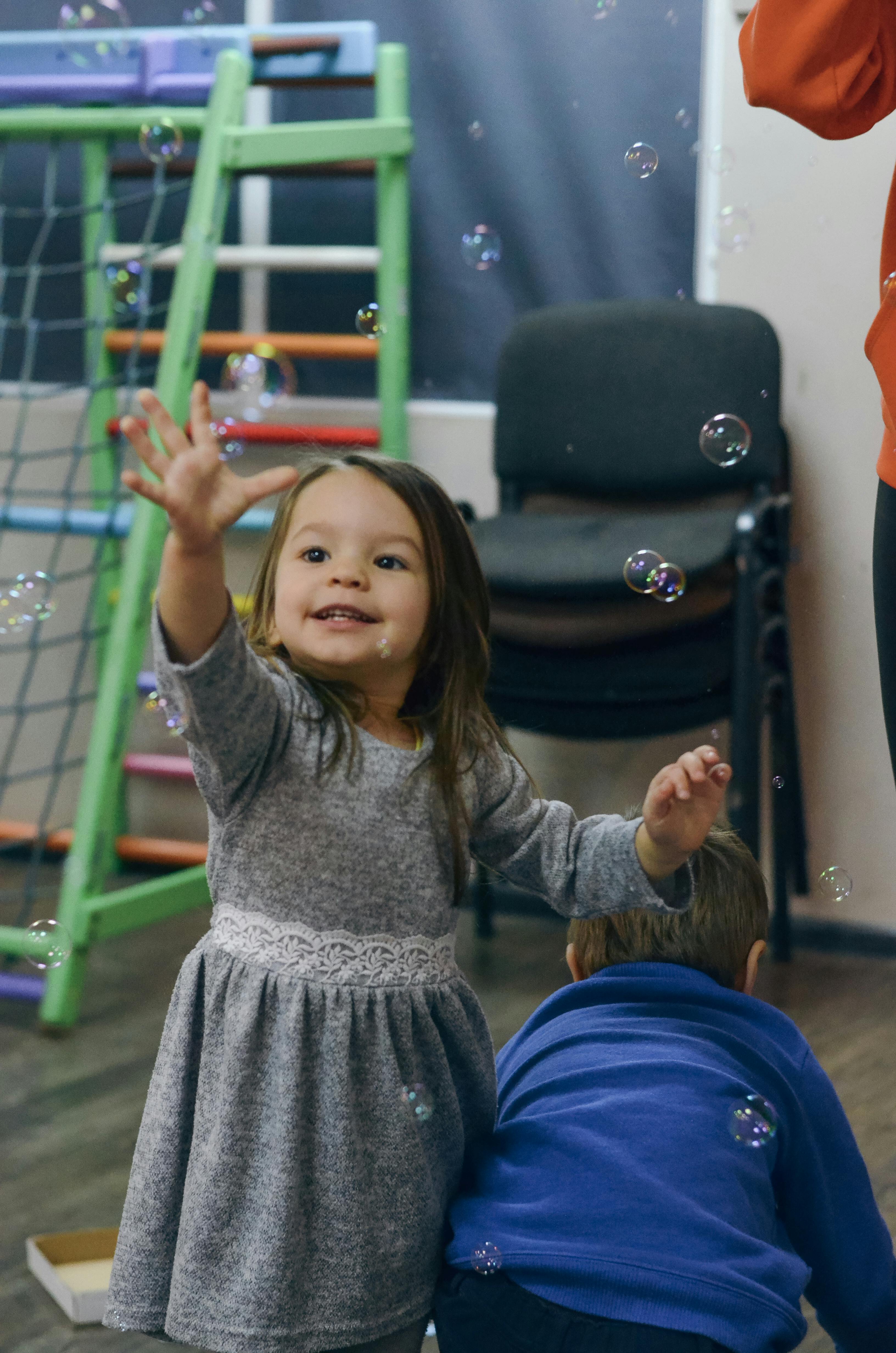 Children having fun blowing and chasing soap bubbles in an indoor play area.
