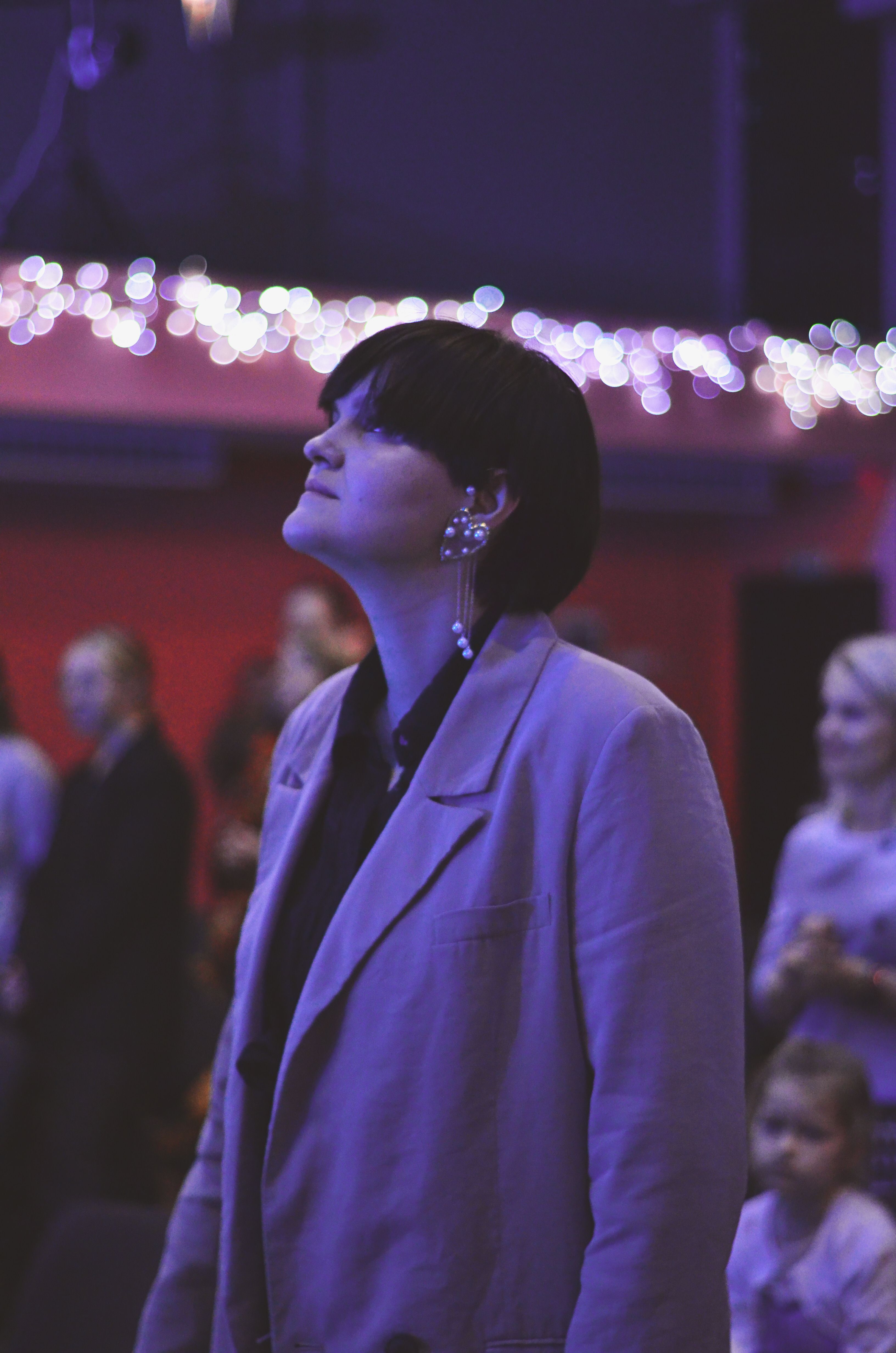 A woman stands attentively in a dimly lit auditorium observing an event.
