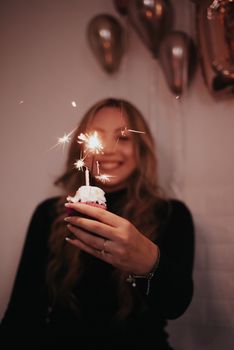 A woman holding a cupcake with sparklers, celebrating a birthday indoors.