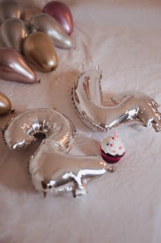A cupcake with a candle beside silver foil balloons forming the number 24 for a birthday celebration.