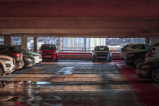 Parked cars in a multi-level parking garage overlooking a cityscape.