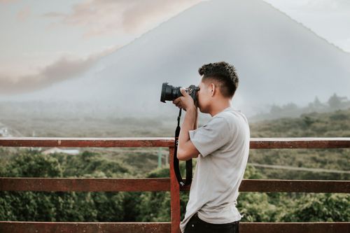 Free An adult male photographer captures a misty mountain landscape using a camera on a wooden deck. Stock Photo