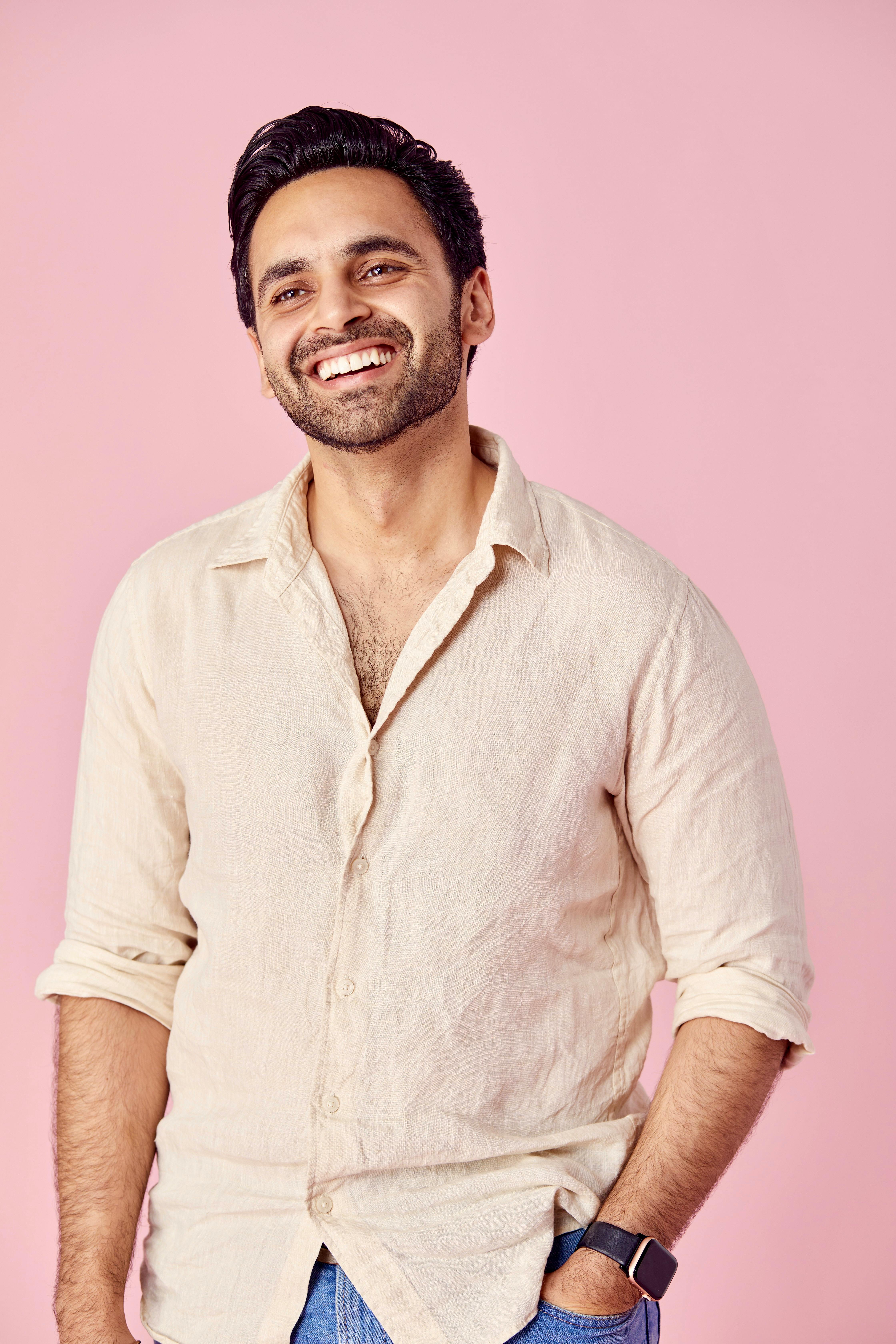 Cheerful man wearing beige shirt, smiling against a pastel pink backdrop. Studio shot.