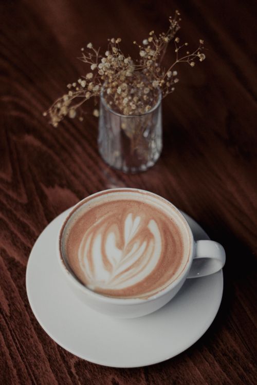 Free A close-up of a cappuccino with intricate latte art by dried flowers, creating a warm cozy atmosphere. Stock Photo