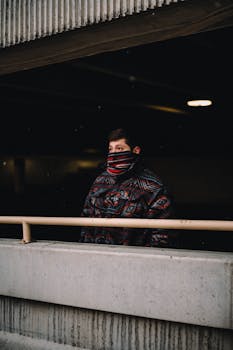 A man with a patterned jacket stands in an urban setting, face partially covered.