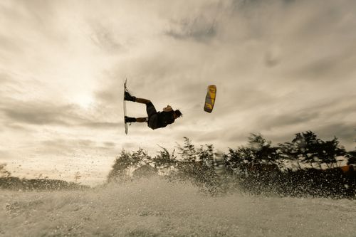 Free A kiteboarder performing a thrilling aerial maneuver over water at sunset, showcasing skill and adventure. Stock Photo