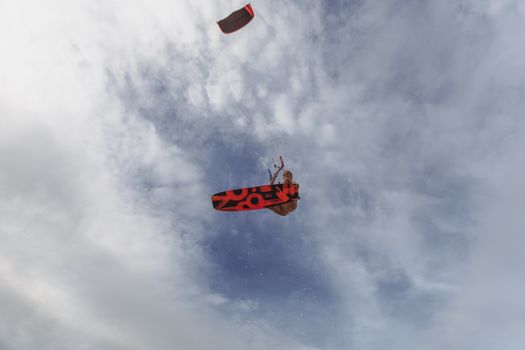 Capture the thrill of kiteboarding with a woman soaring through the sky midair against a vibrant cloudy backdrop.