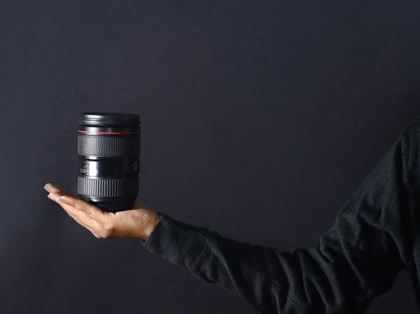 Close-up of a hand holding a camera lens against a dark background.