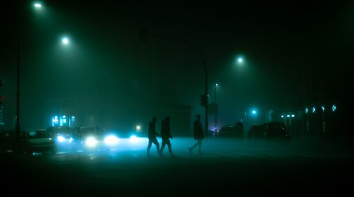 Free Silhouettes of people crossing a foggy street in Rome at night, surrounded by cars and streetlights. Stock Photo