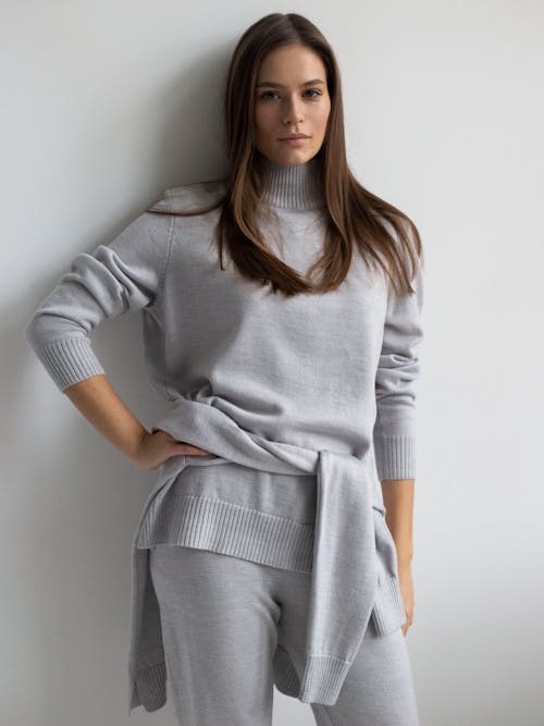 A Woman in Gray Sweater and Pants Leaning on the Wall with Her Hand on Her Waist