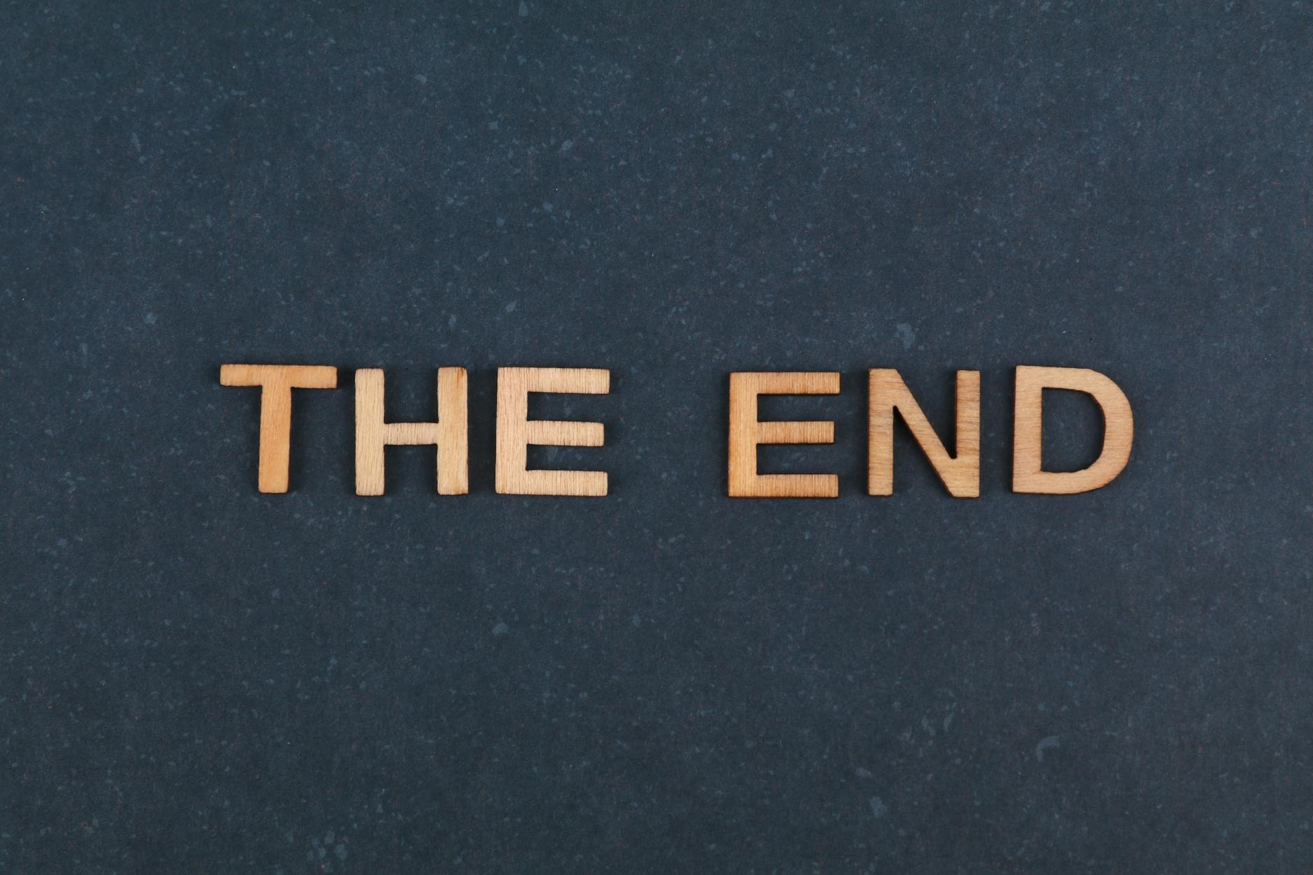 The image displays the phrase 'The End' spelled out in wooden letters against a dark background.