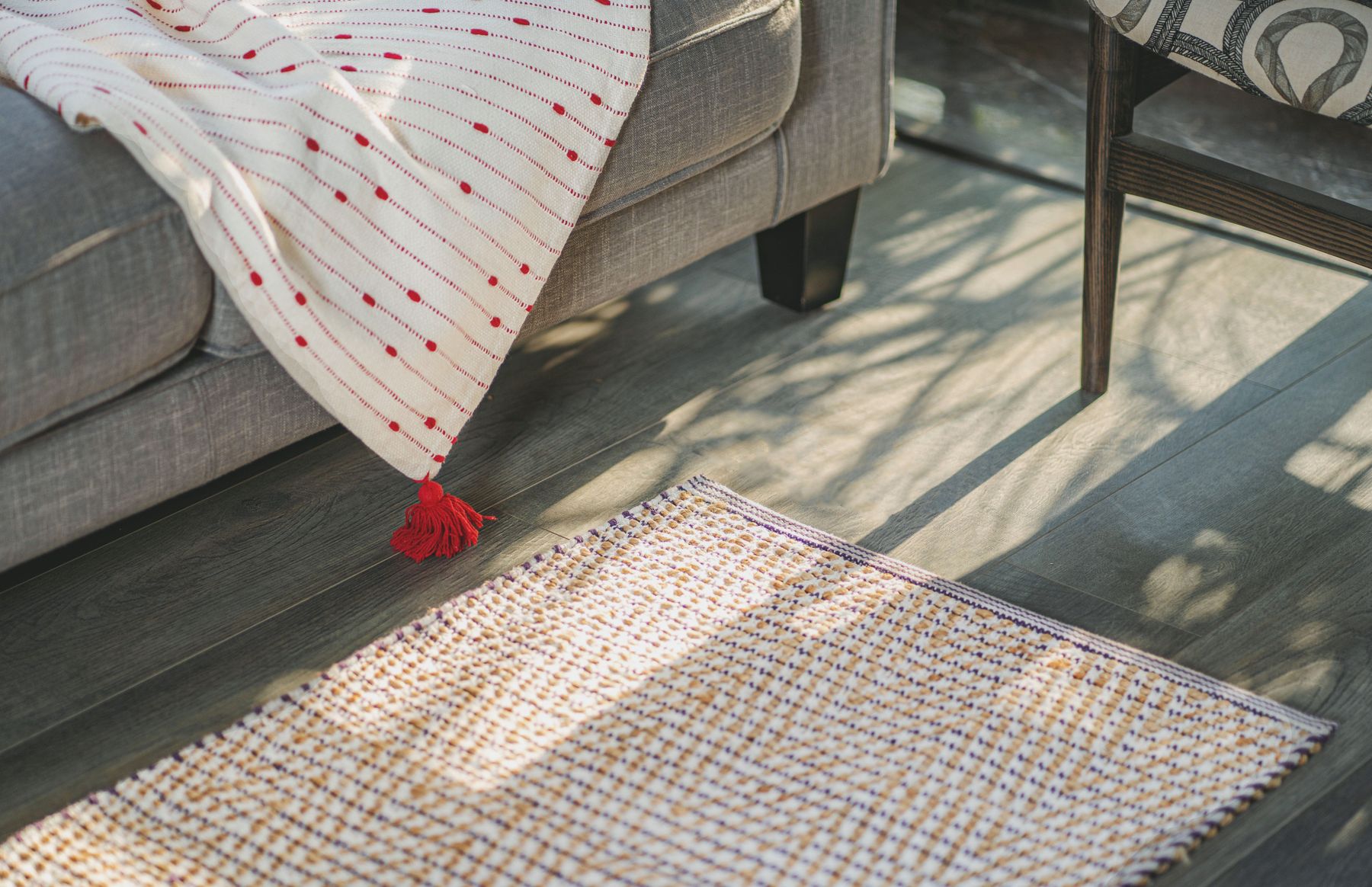 Close view of a woven rug edge near a grey sofa and chair on a wood floor