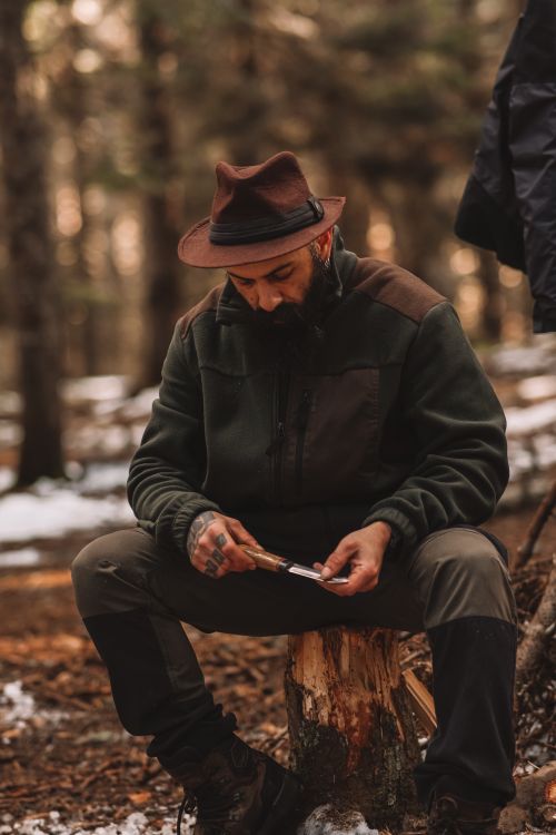 Free A man sharpening a knife on a wooden stump in a wintry forest. Stock Photo