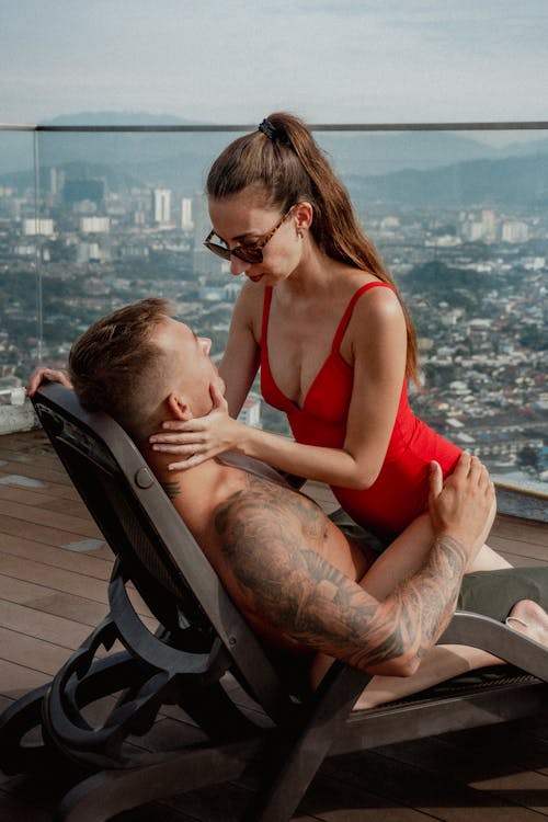 Woman in a Red Swimming Costume and a Shirtless Man Sitting on a Sun Lounger 