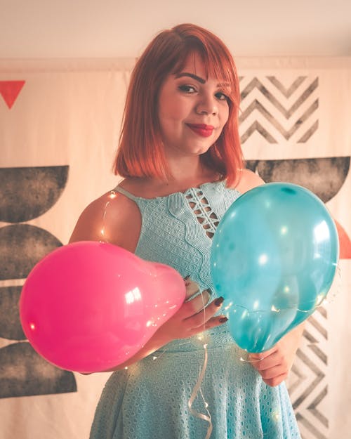 Close-Up Shot of a Redhead Woman in Blue Dress Holding Balloons