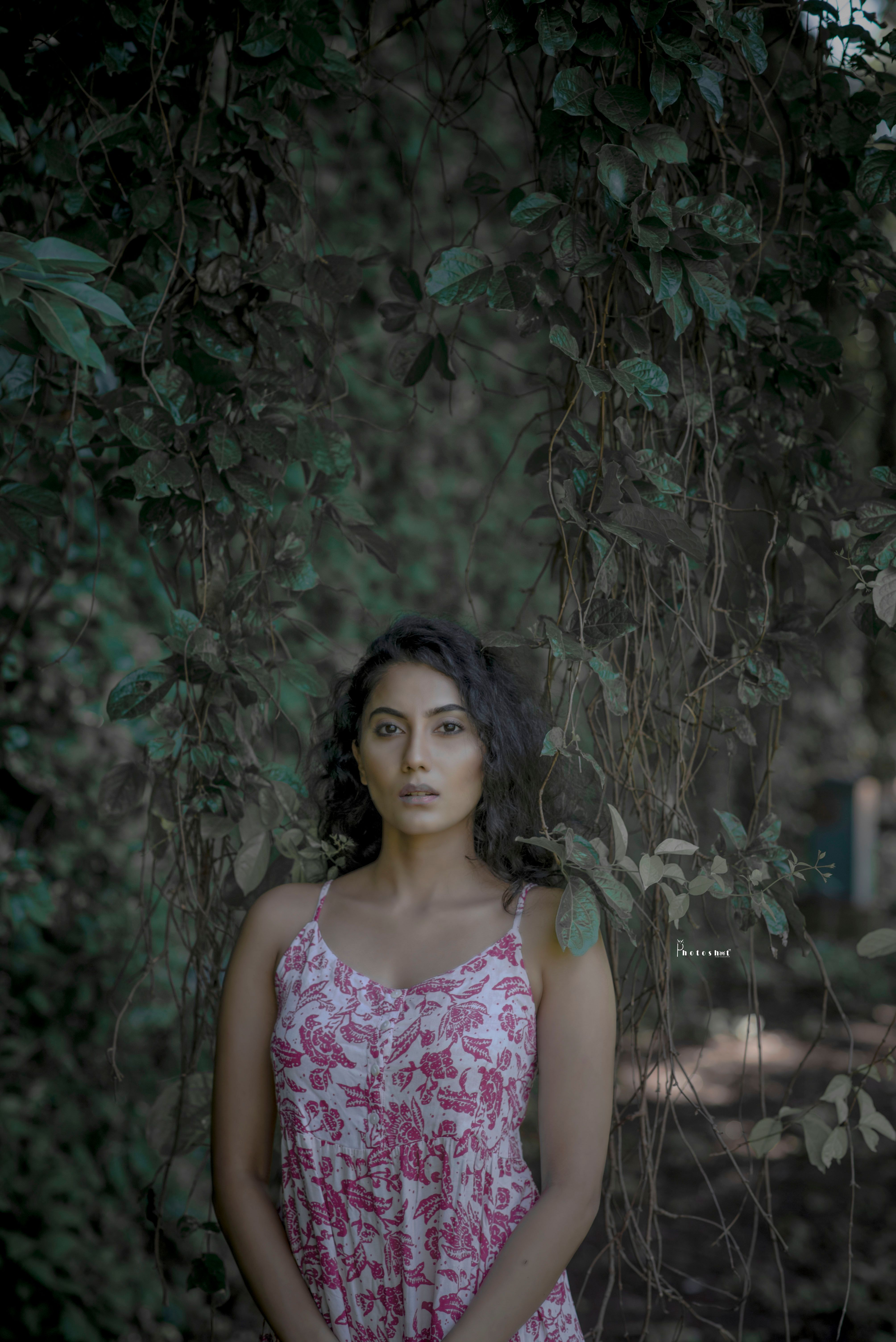 A young woman stands amidst lush greenery, wearing a patterned dress in an outdoor setting, capturing a serene moment.
