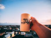 A hand holding a motivational mug with 'Make Mistakes' against a sunset in Lviv.