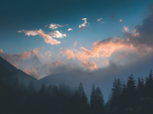 Free A misty mountain range silhouette under a colorful twilight sky with glowing clouds. Stock Photo