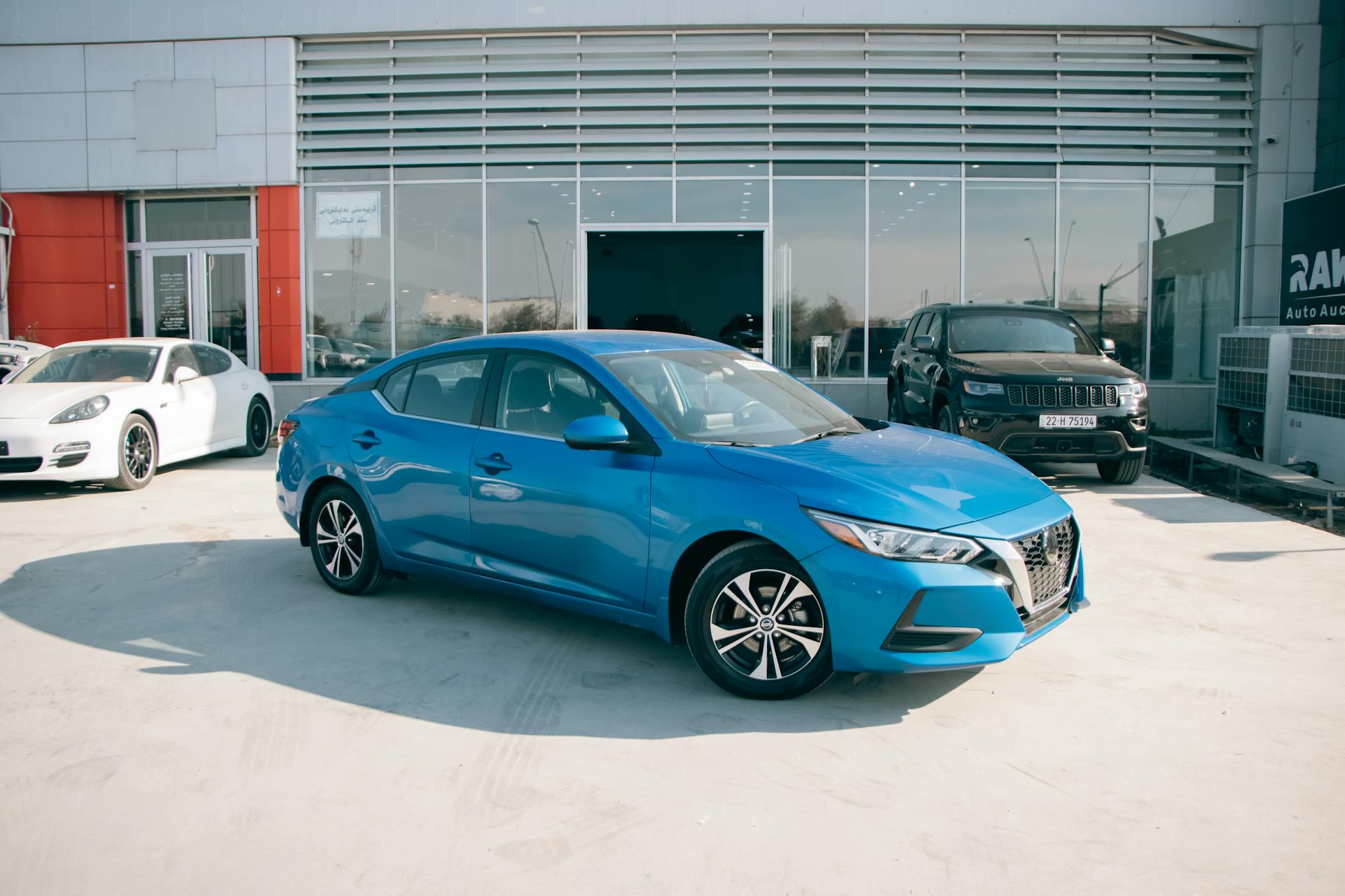 A bright blue Nissan Sentra parked in front of a car dealership on a sunny day.