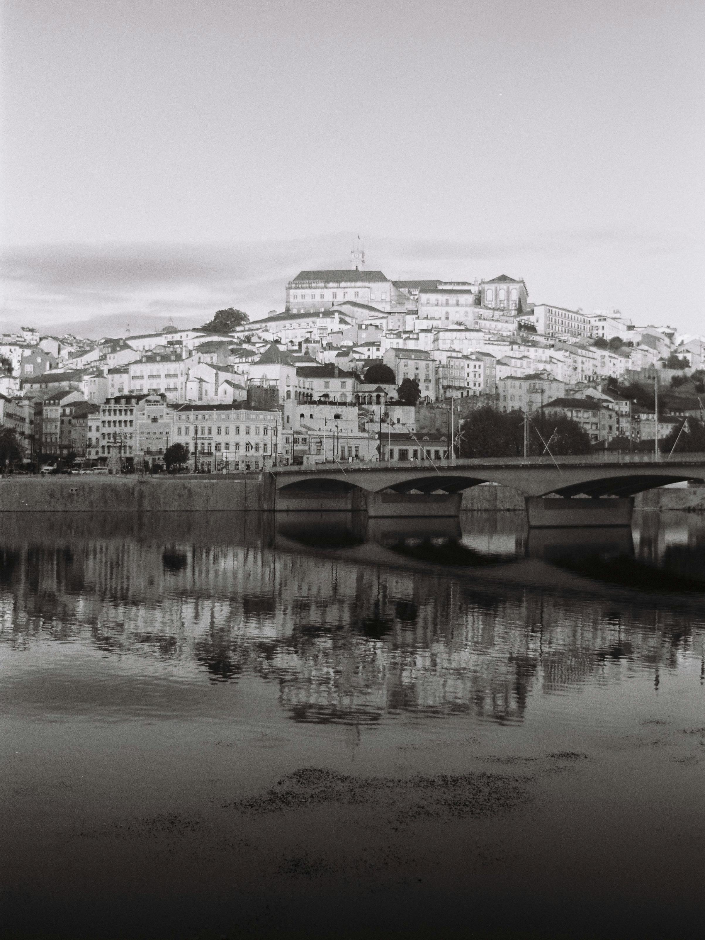 Serene black and white view of Coimbra cityscape reflecting in the Mondego River.