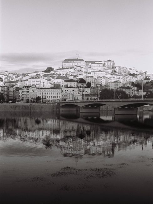 Serene black and white view of Coimbra cityscape reflecting in the Mondego River.