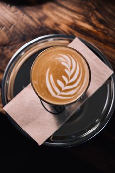 A beautifully crafted cappuccino with latte art displayed on a silver tray on a rustic wooden table.