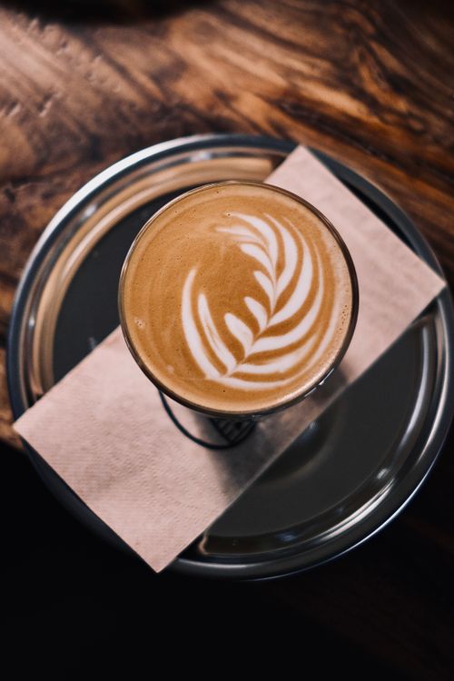 Free A beautifully crafted cappuccino with latte art displayed on a silver tray on a rustic wooden table. Stock Photo
