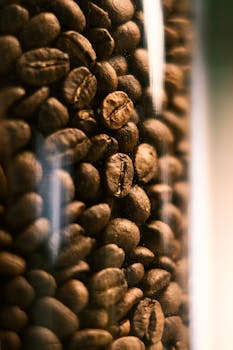 A vertical close-up photo of aromatic roasted coffee beans inside a transparent jar.