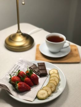 A cozy setting featuring tea, strawberries, chocolate, and sliced fruit on a bedside table.