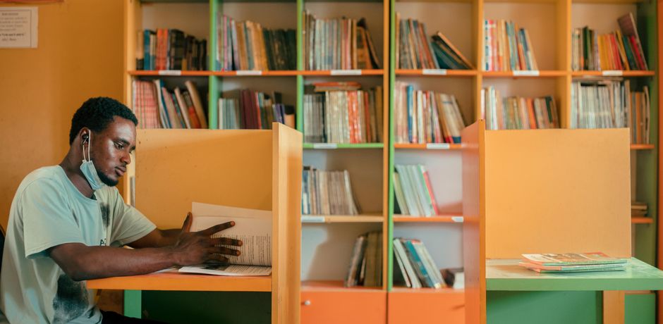 Focused young man studying at a cubicle in a vibrant library, surrounded by books.