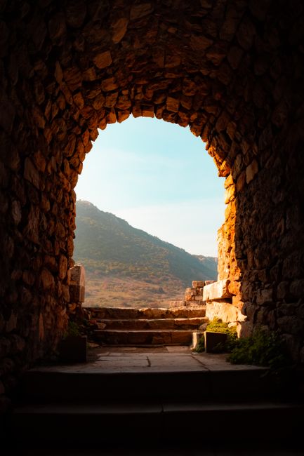 View through an ancient stone archway in İzmir, Türkiye with mountains in the background.