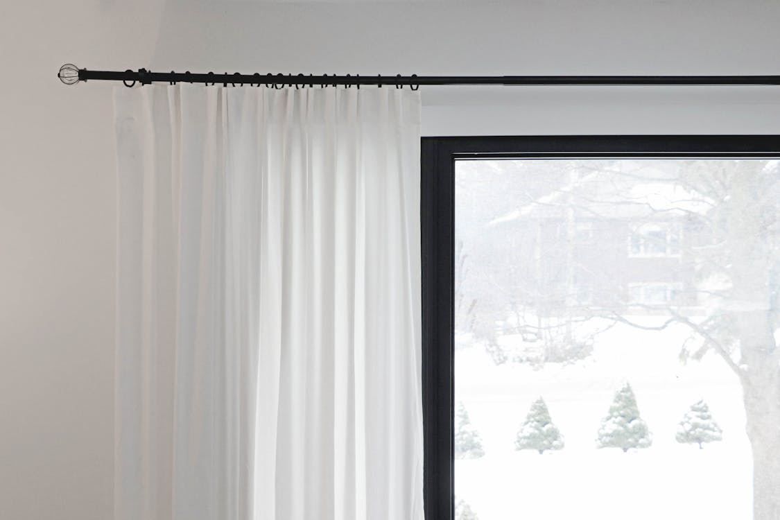 A white curtain with black trim is hanging in front of a window